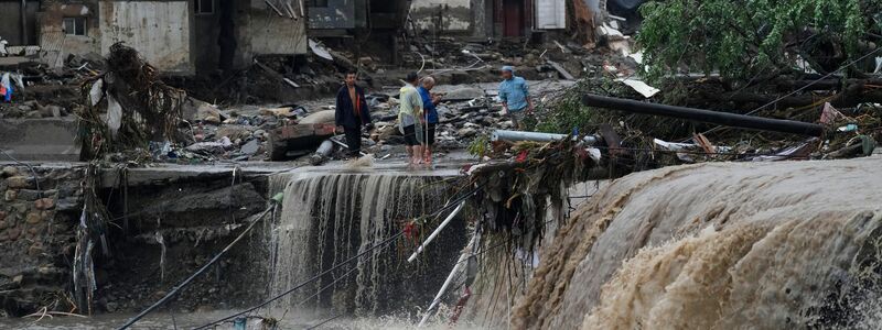 Menschen stehen in Peking vor von den Wassermengen zerstörten Häusern. Die extremen Regenfälle sind eine Folge des Tropensturms «Doksuri». - Foto: Andy Wong/AP/dpa