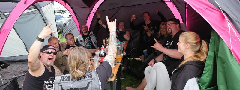 Metal-Fans aus Kiel feiern auf einem Zeltplatz auf dem vom Regen aufgeweichten Festivalgelände. - Foto: Christian Charisius/dpa