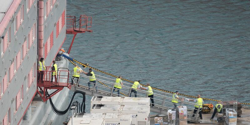 Ein Schleppschiff passiert im Hafen von Portland in Dorset das Schiff «Bibby Stockholm», das bis zu 500 Menschen aufnehmen soll. - Foto: James Manning/PA Wire/dpa