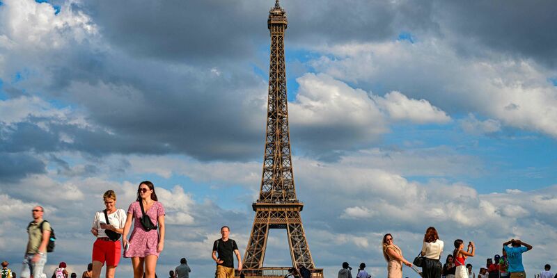 Touristen am Eiffelturm, dem Wahrzeichen der Stadt. Ein Mann ist nach einem Fallschirm-Sprung vom Eiffelturm festgenommen worden. - Foto: Miguel Medina/AFP/dpa