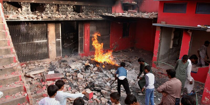 Jugendliche stehen in Jaranwala vor einer Kirche, die beschädigt und niedergebrannt wurde. - Foto: Muhammad Shafqat/AP/dpa
