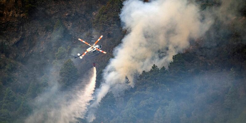 Ein Hubschrauber wirft Wasser auf die Flammen, während sich das Feuer durch den Wald in Richtung der Stadt Pinolere ausbreitet. - Foto: Arturo Rodriguez/AP/dpa