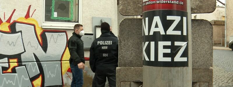 Polizisten stehen vor der Gaststätte «Bull's Eye». An einem Pfahl ist ein Aufkleber mit der Aufschrift «Nazi Kiez» zu sehen. - Foto: Martin Wichmann TV/dpa