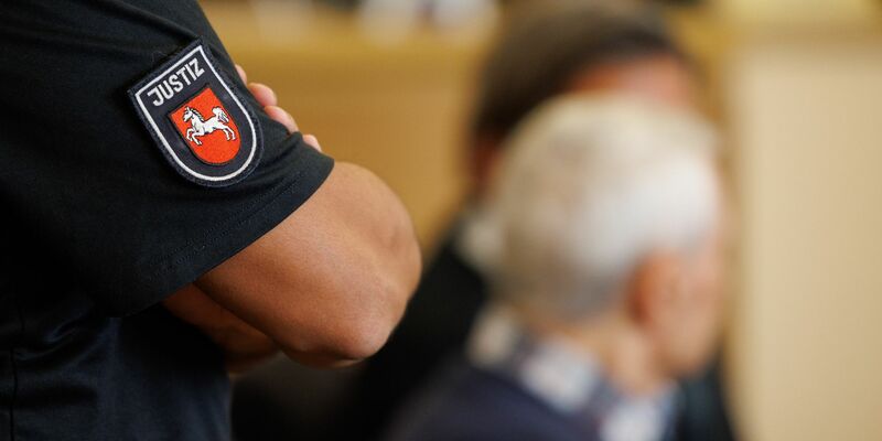 Ein Justizbeamter steht hinter dem Angeklagten im Saal des Landgerichts Osnabrück. - Foto: Friso Gentsch/dpa