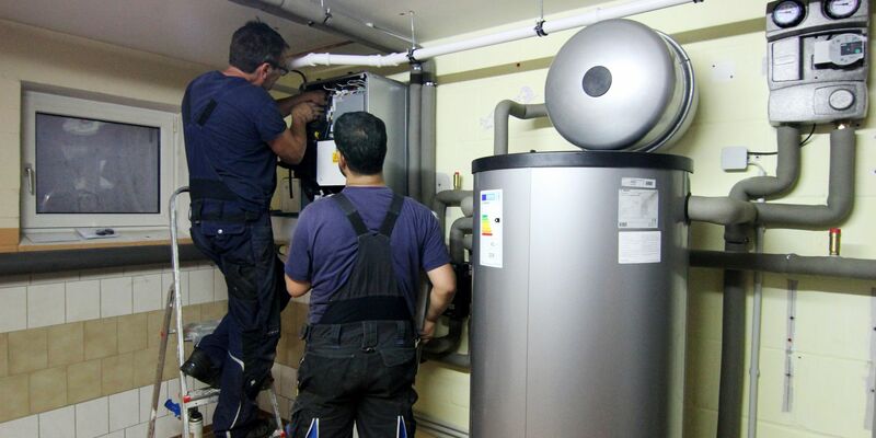 Zwei Handwerker stellen eine gerade installierte Wärmepumpe im Keller einer Doppelhaushälfte ein. - Foto: Doreen Garud/dpa