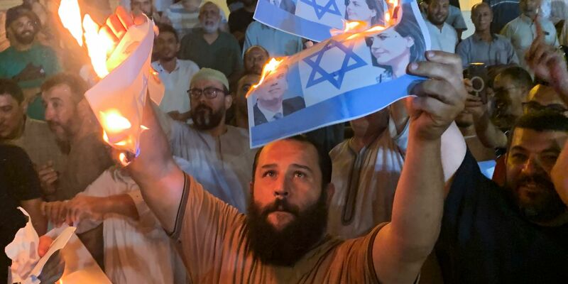 Menschen verbrennen in Tripolis Bilder, die den israelischen Außenminister Eli Cohen und seine libysche Amtskollegin Nadschla al-Mankusch zeigen. - Foto: Yousef Murad/AP