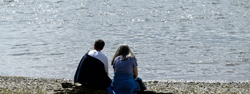 Spaziergänger sitzen am Ufer des Rheins und genießen die Sonne. - Foto: Roberto Pfeil/dpa