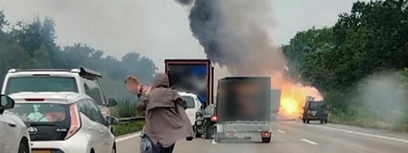 Autofahrer verlassen ihre Fahrzeuge, während im Hintergrund ein Lkw in Flammen steht. Nach einem Auffahrunfall sind auf einem Gefahrguttransporter mehrere Gasflaschen explodiert. - Foto: -/TNN/dpa