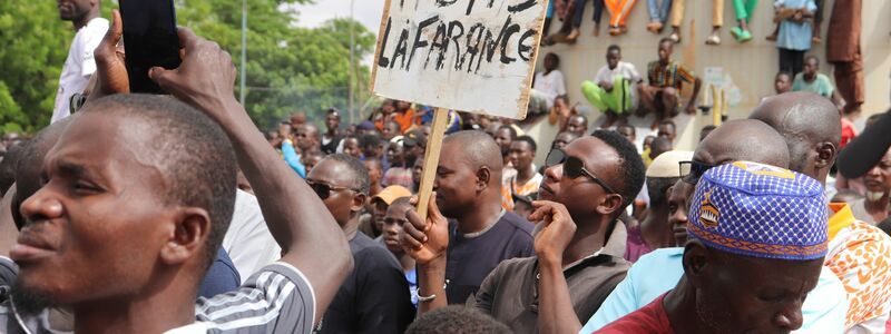 Menschen demonstrieren am 03.08.2023 in Nigers Hauptstadt Niamey, um damit ihre Unterstützung für die Putschisten zu zeigen. Ein junger Mann hält dabei ein Schild mit der Aufschrift «A bas la France» (Nieder mit Frankreich) in die Höhe. - Foto: 1