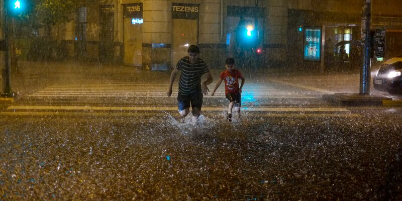 Menschen überqueren bei starkem Regen eine überschwemmte Straße in Pamplona. - Foto: Alvaro Barrientos/AP