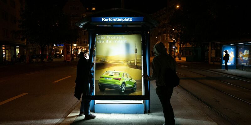 Aktivisten von Attac bringen als Protest gegen die IAA kritische Persiflagen von Autowerbung an einem Trambahnhäuschen an. - Foto: Lukas Barth/dpa