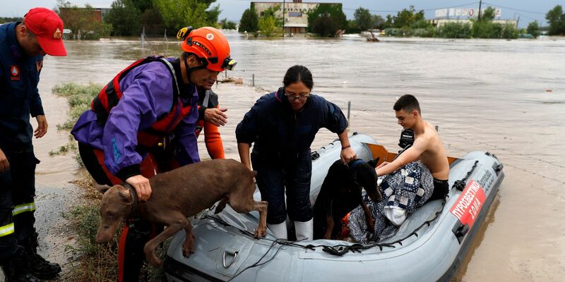 Feuerwehrleute mit einem Schlauchboot evakuieren Menschen und ihre Hunde aus überfluteten Gebäuden. - Foto: Vaggelis Kousioras/AP/dpa