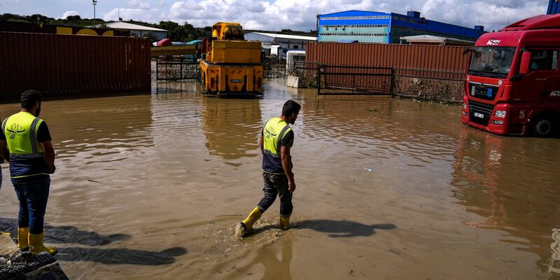 Arbeiter laufen nach Überschwemmungen durch schwere Regenfälle durch das Hochwasser. - Foto: Khalil Hamra/AP/dpa