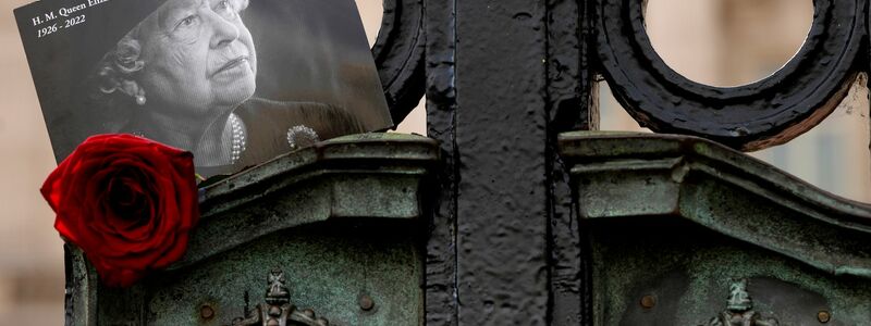 Ein Foto von Königin Elizabeth II. hängt am Tor des Buckingham Palace in London. Mit Salutschüssen und Glockengeläut gedenkt Großbritannien des ersten Jahrestages des Todes von Königin Elizabeth II. - Foto: Kirsty Wigglesworth/AP/dpa