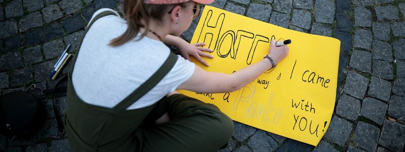Eine junge Frau schreibt auf ein Schild: «Harry, I came all the way to take a photo with you!» - Foto: Fabian Strauch/dpa