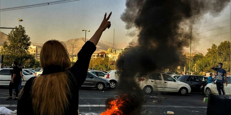 Eine Frau steht während einer Demonstration in Teheran vor einem brennenden Autoreifen und zeigt das Victory-Zeichen. - Foto: Uncredited/AP/dpa