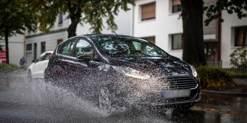 Nach starken Regenfällen am Dienstagmorgen fährt ein Auto durch eine große Pfütze in Duisburg. - Foto: Christoph Reichwein/dpa
