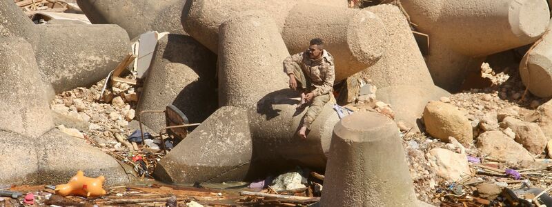 Ein Mann sitzt auf einem Wellenbrecher und blickt auf einen Teil der Schäden. - Foto: Yousef Murad/AP/dpa