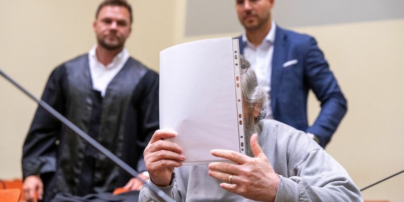 Der Angeklagte hält sich im Gerichtssaal ein Blatt Papier vor das Gesicht. Im Hintergrund stehen seine Anwälte. - Foto: Peter Kneffel/dpa