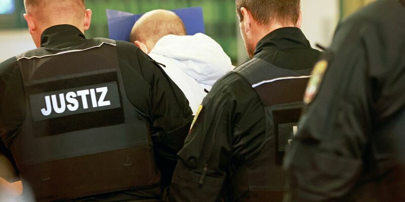 Der wegen Mordes angeklagte Mann (M) versteckt auf dem Weg in den Gerichtssaal sein Gesicht. - Foto: Matthias Bein/dpa