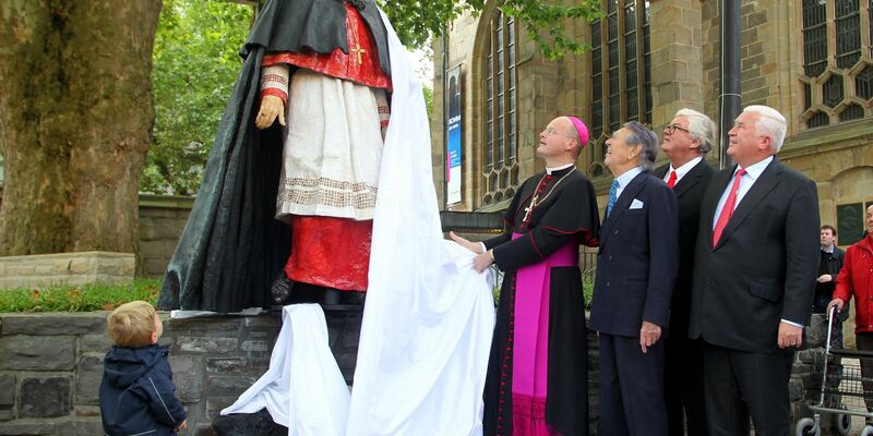 Franz-Josef Overbeck (l) enthüllt 2011 mit Gästen die Skulptur für den verstorbenen Franz Kardinal Hengsbach. - Foto: Roland Weihrauch/dpa