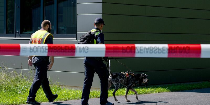 Polizeibeamte ermitteln mit einem Spürhund am Schulzentrum in Lohr am Main, wo der tote 14-Jährige gefunden wurde. - Foto: Pia Bayer/dpa