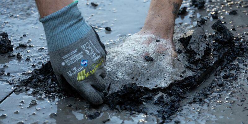 Ein Polizist entfernt Asphalt, um einen Aktivisten von der Straße zu lösen. - Foto: Hannes P. Albert/dpa