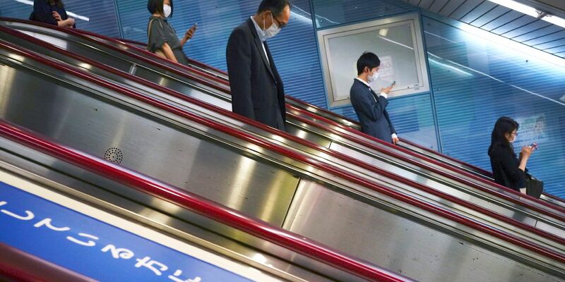 Menschen fahren auf einer Rolltreppe in eine U-Bahn-Station in Tokio. - Foto: Eugene Hoshiko/AP/dpa