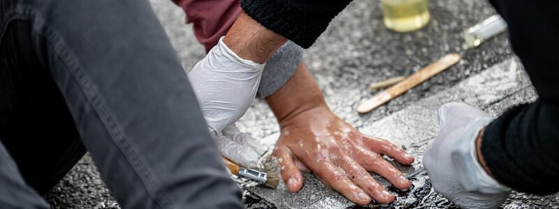 Eien Aktivistin der Letzten Generation hat sich auf die Straße geklebt. Ein Polizist versucht, ihre Hand vom Asphalt zu lösen. - Foto: Fabian Sommer/dpa
