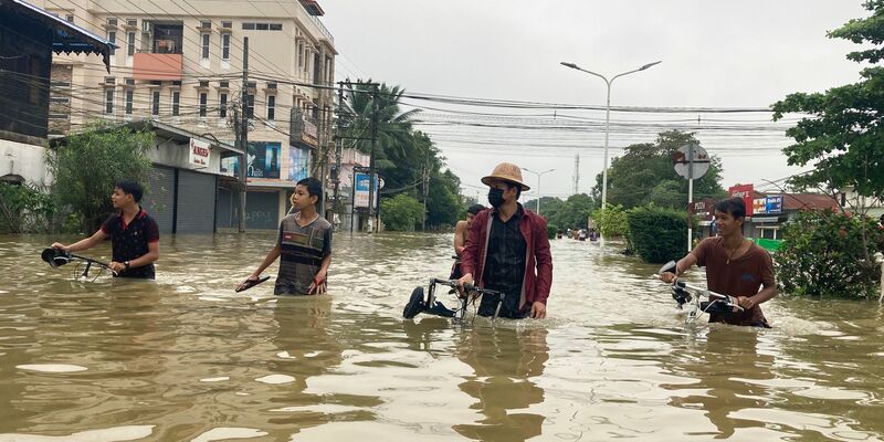 Anwohner schieben ihre Fahrräder durch eine überschwemmte Straße in Bago. - Foto: Thein Zaw/AP/dpa