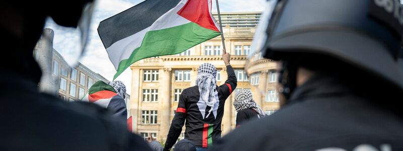 Ein Teilnehmer einer verbotenen Pro-Palästina-Demonstration in Frankfurt am Main schwenkt eine Palästina-Flagge, während Polizisten die Situation beobachten. - Foto: Hannes P. Albert/dpa