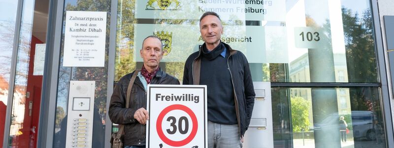 Christian Kronbitter (l) und Erich Maier vor dem Verwaltungsgericht in Freiburg mit einem «Freiwillig 30»-Schild. - Foto: Silas Stein/dpa