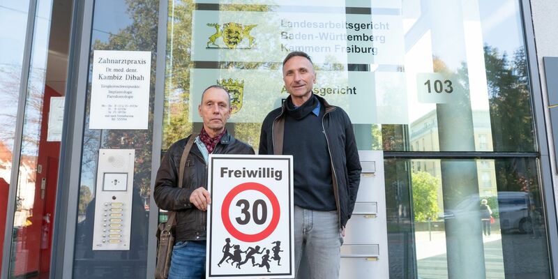 Christian Kronbitter (l) und Erich Maier vor dem Verwaltungsgericht in Freiburg mit einem «Freiwillig 30»-Schild. - Foto: Silas Stein/dpa