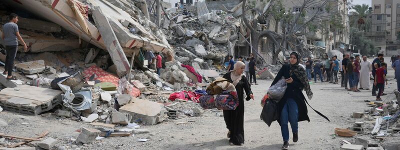 Palästinensische Frauen gehen in Nuseirat im Gazastreifen an Gebäuden vorbei, die bei israelischen Luftangriffen zerstört wurden. - Foto: Hatem Moussa/AP/dpa