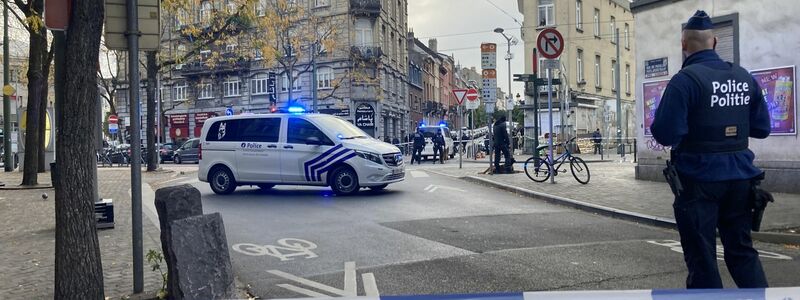 Die Polizei sperrt eine Straße, während ein Polizist hinter Absperrband Wache steht. - Foto: Lou Lampaert/Belga/dpa