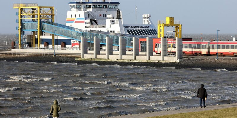 Spaziergänger sind bei stürmischem Wetter am Hafen von Dagebüll unterwegs. (Archivbild) - Foto: Bodo Marks/dpa