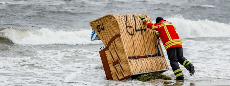 Ein Feuerwehrmann versucht, in Kiel-Schiksee einen Strandkorb vor den Flutwellen der Ostsee zu sichern. - Foto: Axel Heimken/dpa