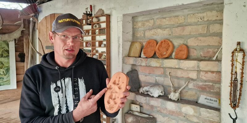 Wildnispädagoge Paul Wernicke zeigt in seiner Wildnisschule in Bad Belzig den Pfotenabdruck eines Wolfes in Ton. - Foto: Cevin Dettlaff/dpa-Zentralbild/dpa