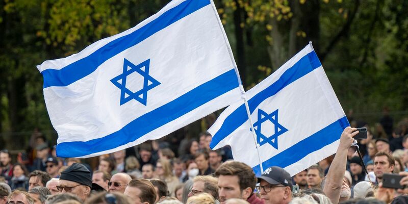Teilnehmer der Kundgebung „Aufstehen gegen Terror, Hass und Antisemitismus – in Solidarität und Mitgefühl mit Israel“ stehen umhüllt in eine israelische Flagge vor dem Brandenburger Tor in Berlin. - Foto: Monika Skolimowska/dpa