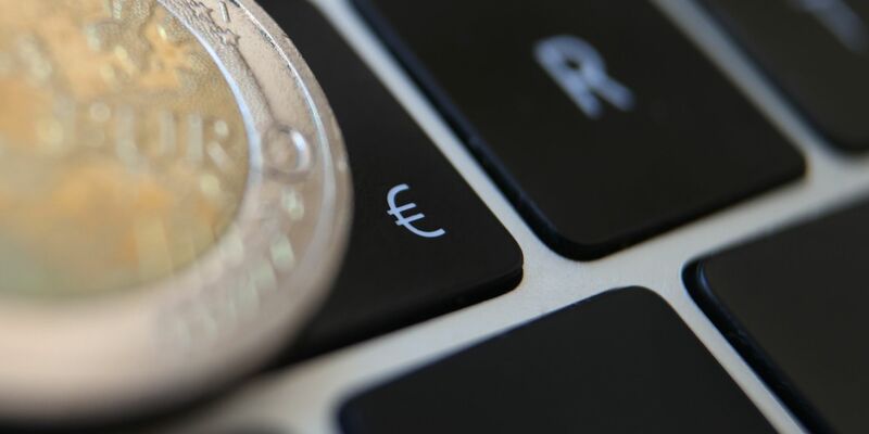 Eine Zwei-Euro-Münze liegt auf der Tastatur eines Laptops neben einem Eurozeichen. Die EBZ hebt die Zinsen vorerst nicht weiter an. (Symbolbild) - Foto: Karl-Josef Hildenbrand/dpa