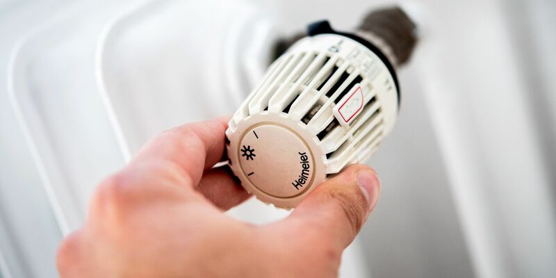 Ein Mann dreht in einer Wohnung am Thermostat einer Heizung. - Foto: Hauke-Christian Dittrich/dpa
