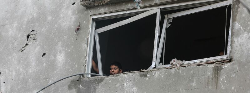 Ein kleiner palästinensischer Junge blickt aus dem Fenster eines zerstörten Gebäudes. - Foto: Mohammed Talatene/dpa
