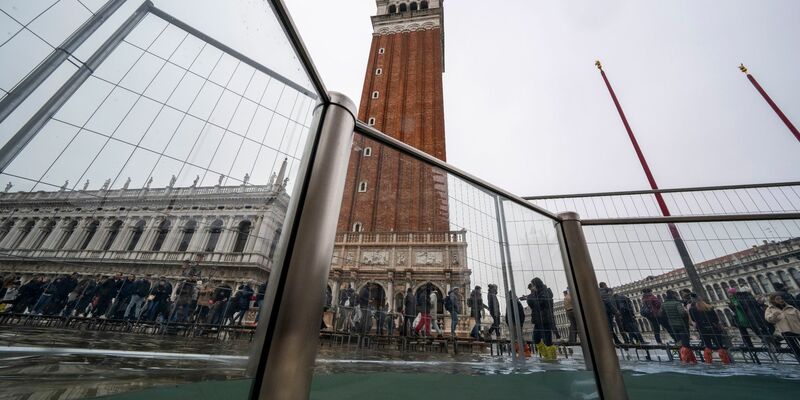 Touristen gehen auf Laufstegen über den überschwemmten Markusplatz. - Foto: Domenico Stinellis/AP/dpa