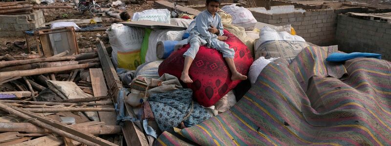 Ein afghanischer Junge sitzt auf den Habseligkeiten seiner Familie, die aus beschädigten Lehmhäusern geholt wurden. - Foto: Anjum Naveed/AP/dpa