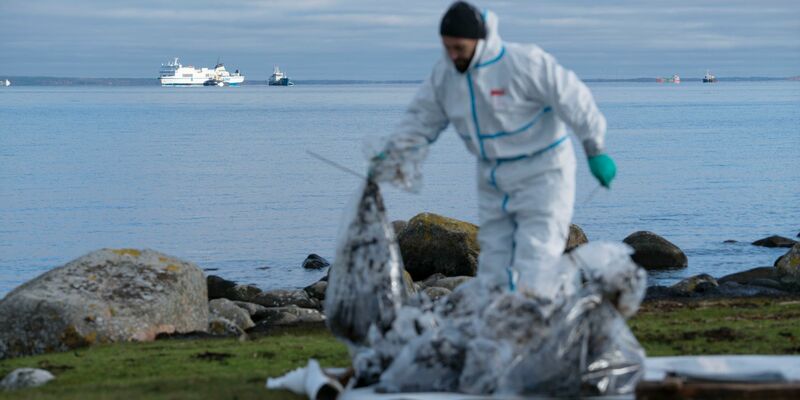 Ein Mann in Schutzkleidung arbeitet am Strand. Bei der vor der südschwedischen Küste feststeckenden Ostseefähre «Marco Polo» (hinten, l) ist erneut Öl ausgetreten. - Foto: Ola Torkelsson/TT News Agency/AP/dpa