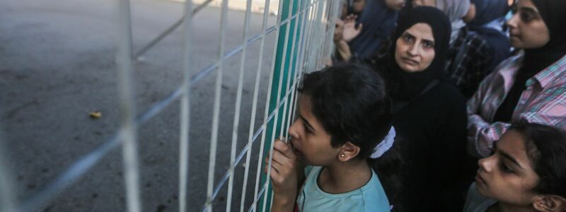 Menschen warten vor einem Zaun am Grenzübergang zwischen dem Gazastreifen und Ägypten. - Foto: Mohammed Talatene/dpa