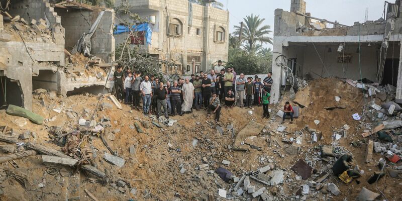 Palästinenser stehen in Chan Junis im Gazastreifen um einen Krater herum, der durch einen israelischen Angriff verursacht wurde. - Foto: Mohammed Talatene/dpa
