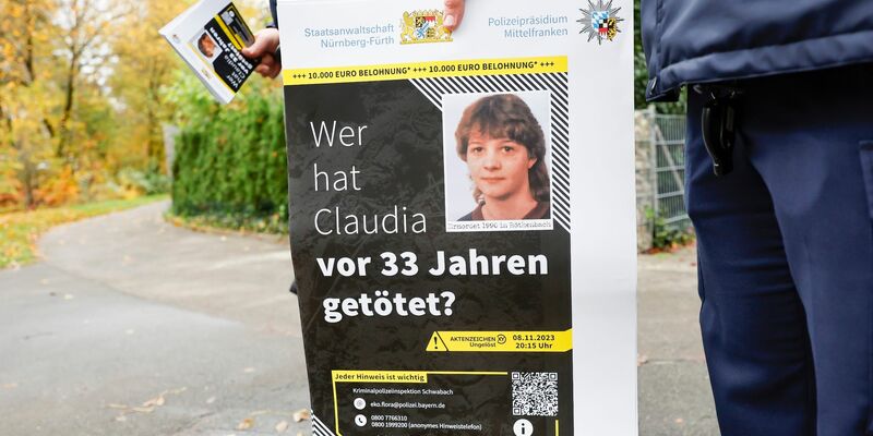 Ein Polizist mit einem Plakat zum Mordfall von 1990 in Röthenbach an der Pegnitz. - Foto: Daniel Löb/dpa