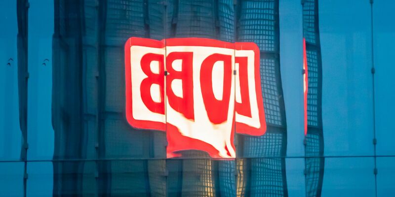 Das Logo der Deutschen Bahn AG (DB) am Berliner Hauptbahnhof spiegelt sich am Morgen in einer Gebäudefassade. - Foto: Christoph Soeder/dpa