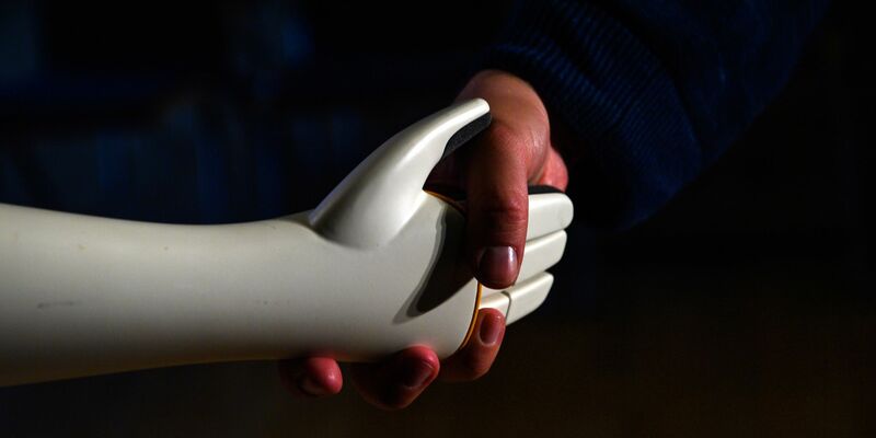 Eine menschliche Hand greift die Hand eines humanoiden Roboters. - Foto: Klaus-Dietmar Gabbert/dpa